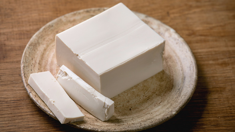 A block of silken tofu with two slices rests on a plate