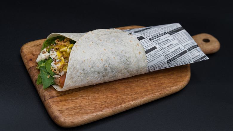 Burrito wrapped in newspaper on a wooden board