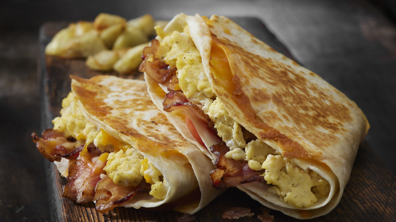 Folded breakfast quesadilla on a wooden tray with eggs, bacon, and cheese inside