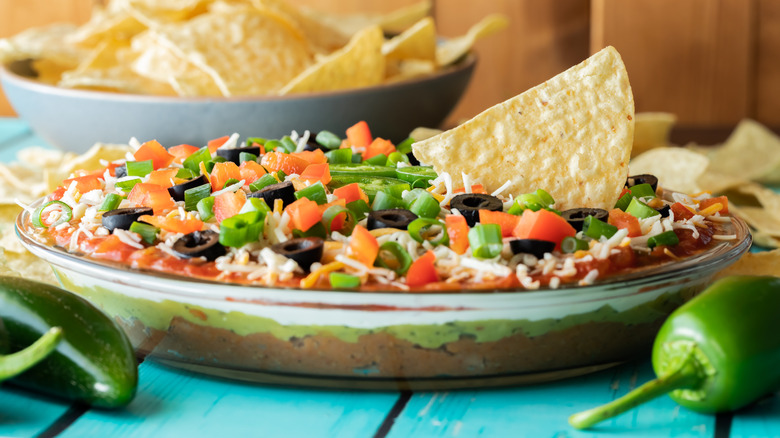 Many layered bean dip with diced tomatoes, black olives, green onions, and guacamole