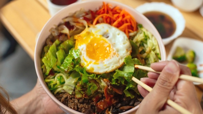 A bowl of bibimbap with fresh vegetables and an egg