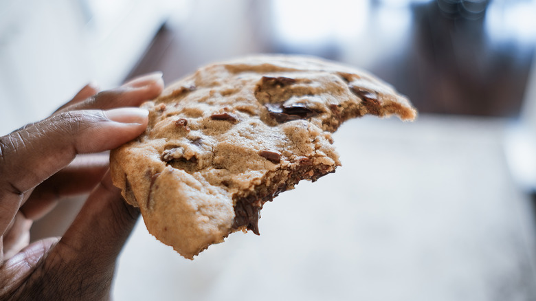 A person holding a large half-eaten chocolate chip cookie