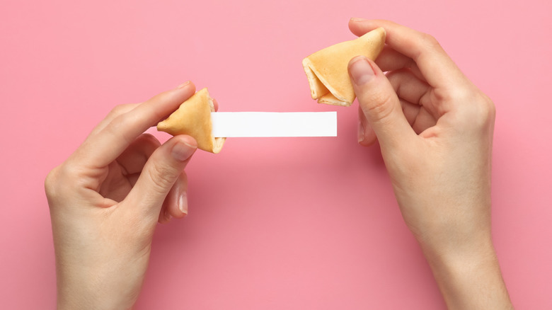 A person opens a fortune cookie with a message inside