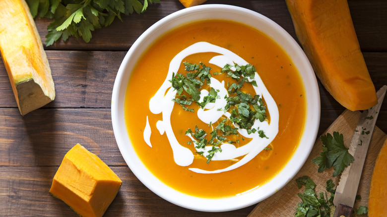pumpkin soup garnished with cream and parsley on a bowl on a table