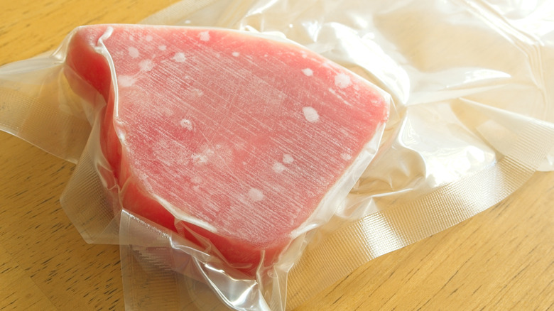 Frozen ahi tuna in a vacuum-sealed package rests on a wooden surface.