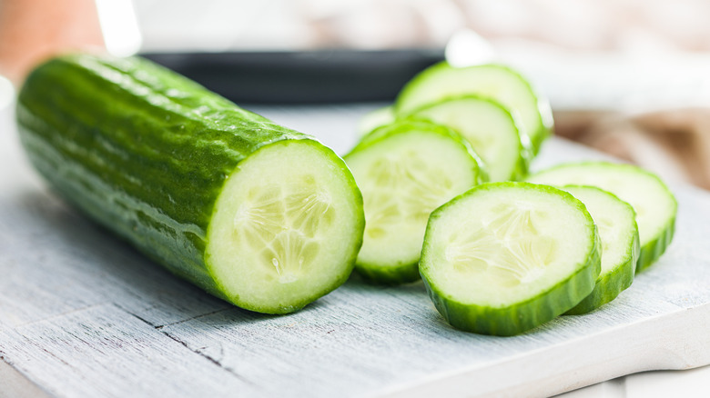 A sliced cucumber on cutting board next to cucumber slices