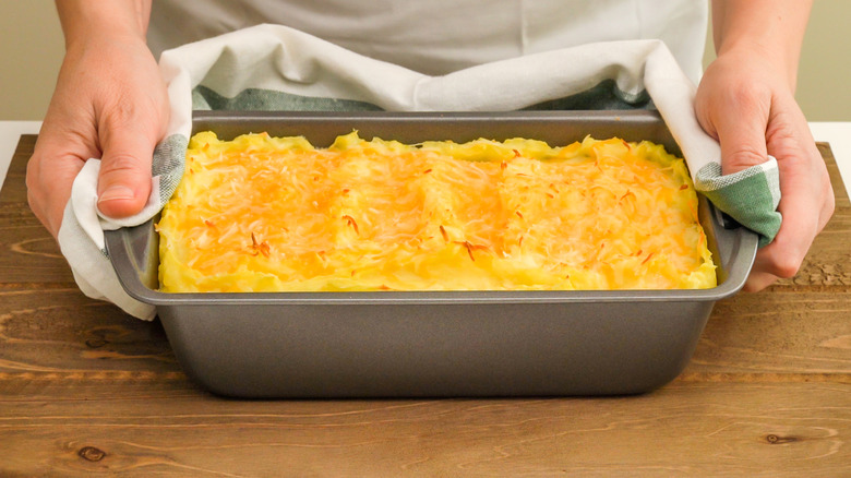 Hands placing cooked casserole on cutting board