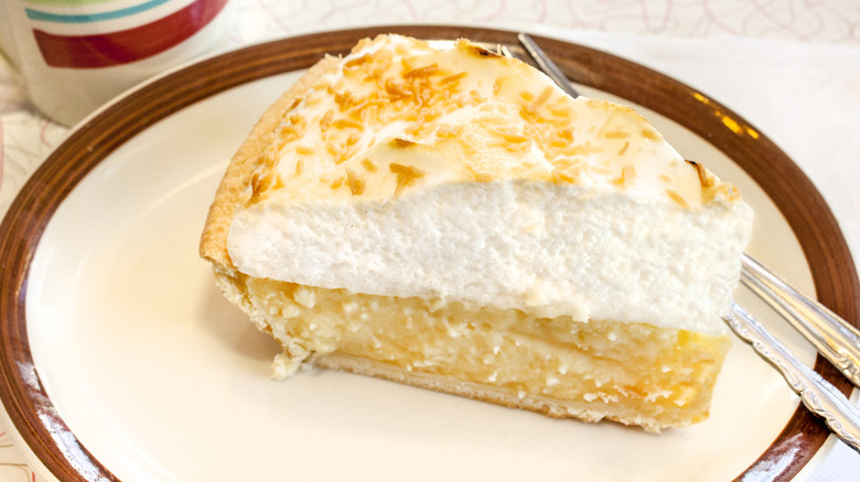 Slice of pie with thick meringue top on a white diner plate with brown trim.