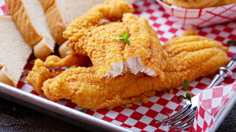 Fried catfish on a metal serving tray covered with white and red checkered paper.