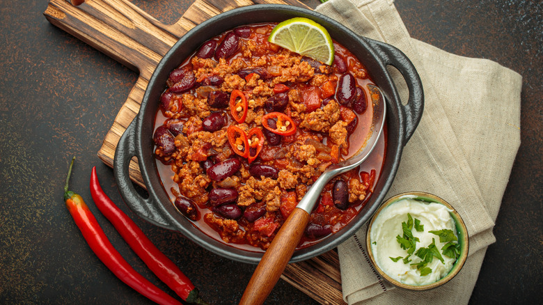 Cast iron pot full of chili topped with sliced peppers and a lime wedge.