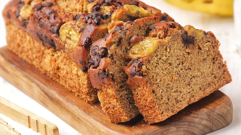 Sliced loaf of banana bread on wooden cutting board.