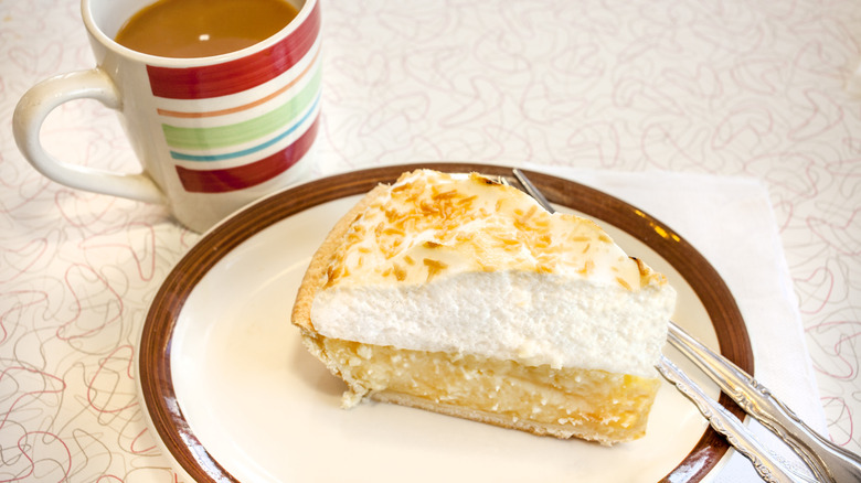 A plate of coconut cream pie on a table with a cup of coffee next to it