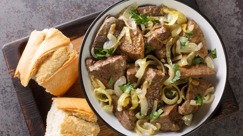Homemade food fried beef liver with onions and herbs close-up in a plate and bread on a wooden tray on the table