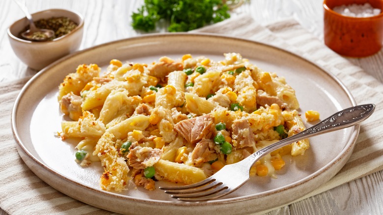 Tuna Mornay, Creamy Tuna Casserole Penne Pasta Bake on plate on white wooden table with fork, landscape view