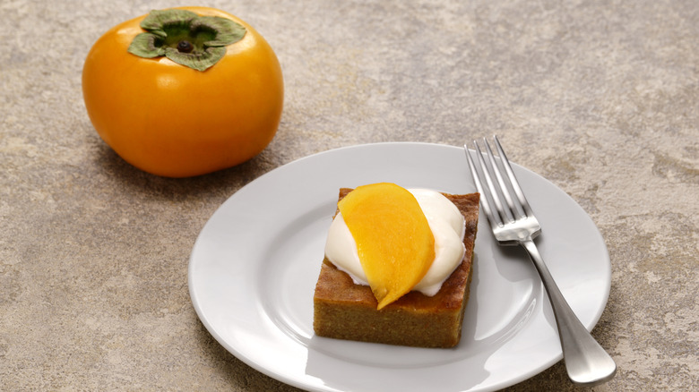 Slice of Persimmon Pudding Topped with Cream and on Plate with Fresh Persimmon