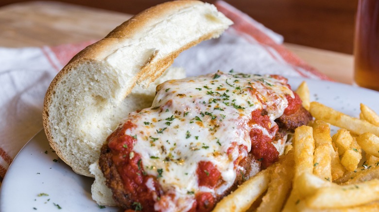 Delicious Italian sandwich and fries served on white plate with a bistro style napkin and birch table.