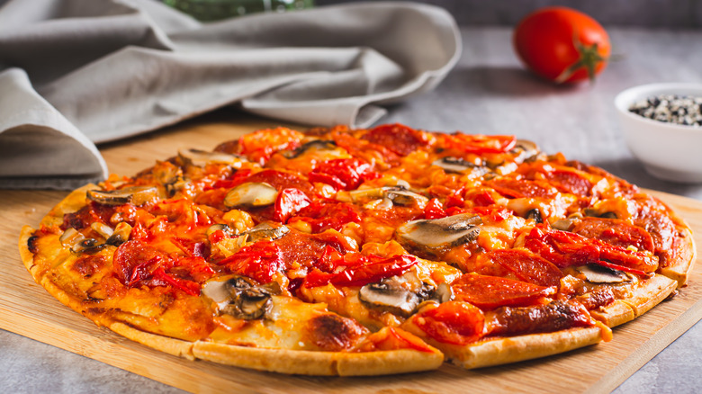St. Louis Style pizza with bacon, mushrooms, tomatoes and peppers on a board on the table