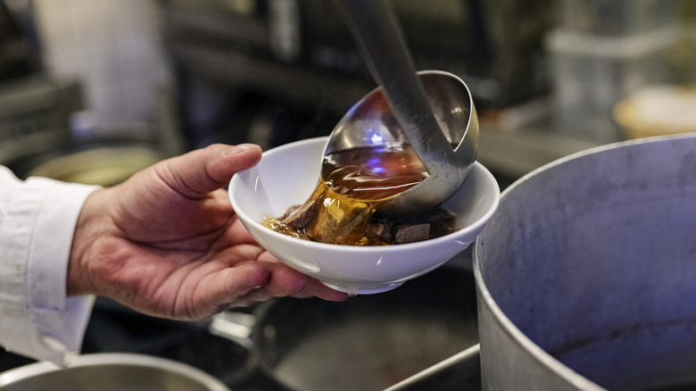 Chef ladling consomme into a white bowl