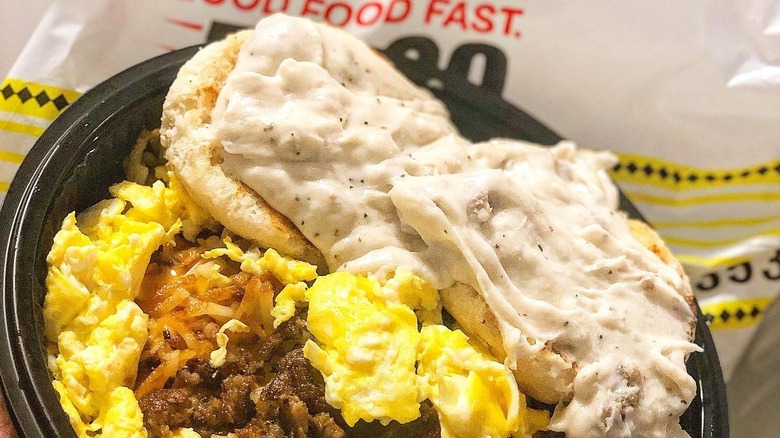 A plate of Waffle House biscuits covered with gravy and sitting on a bed of eggs, sausage and hash browns.