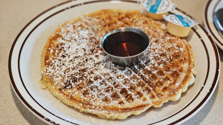 Waffle House waffle on a plate with powdered sugar dusted on and butter and syrup accompanied