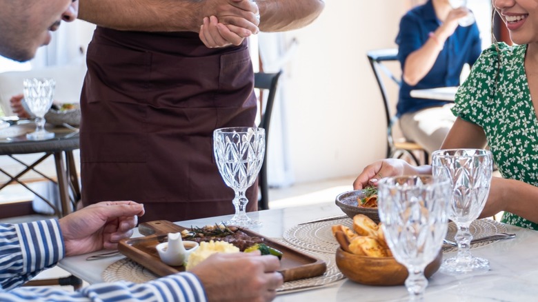 A restaurant server at a table with two patrons