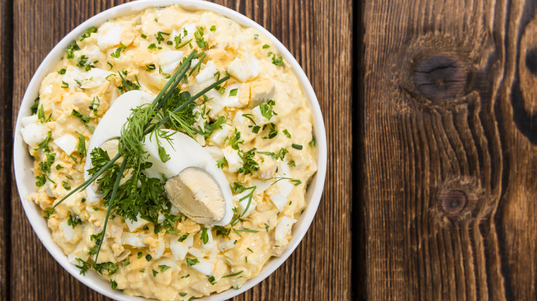 A bowl of egg salad garnished with hard boiled egg quarters and fresh herbs