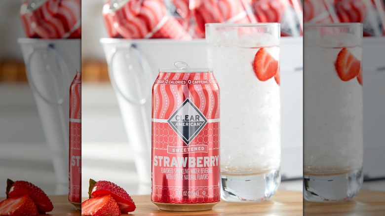 A can of Strawberry Clear American sparkling water from Walmart styled with a glass, fresh strawberries, and a bucket of cans
