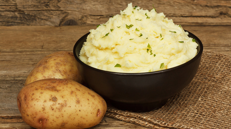 A serving of creamy mashed potato made from boiled potatoes mixed with butter and served in a black bowl on a traditional rustic background.