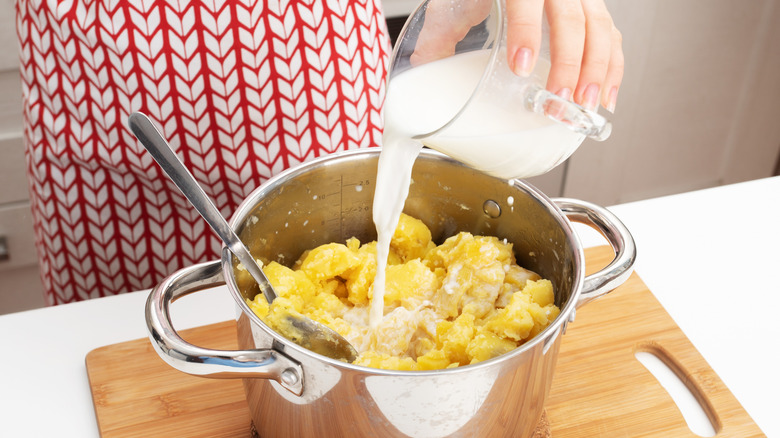 Female hands add milk to the pan while cooking mashed potatoes.