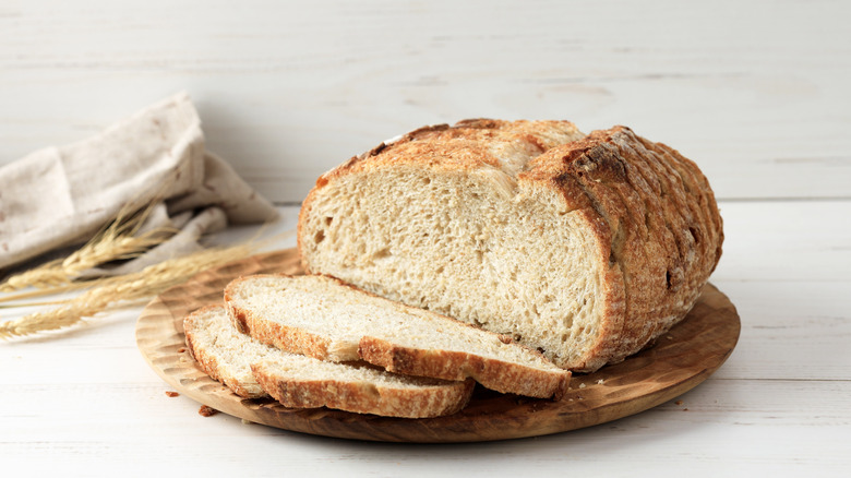 A loaf of sourdough bread sliced into thin pieces on a round wooden board
