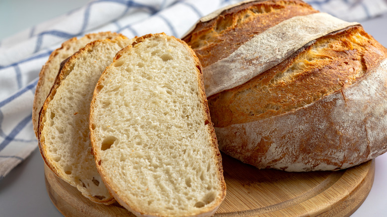 A full loaf of sourdough bread beside three soft pieces of sourdough bread on a wooden surface