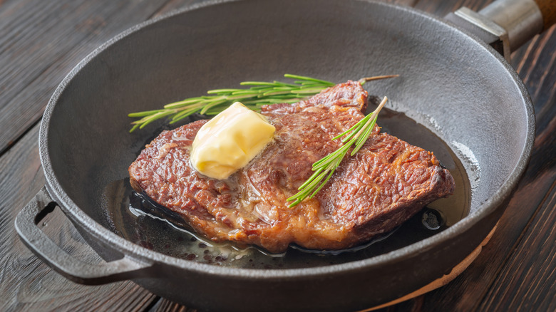 A piece of caramelized steak with a large piece of butter on it sitting in a pan.