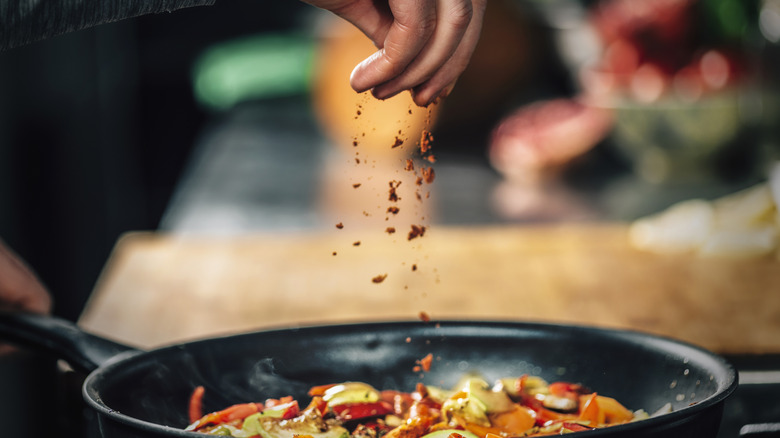 A hand sprinkling paprika over a pan of vegetables as they roast