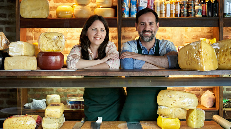 Two people smiling and standing behind a cheese counter