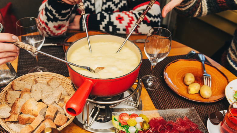 People dipping foods into cheese fondue pot at table