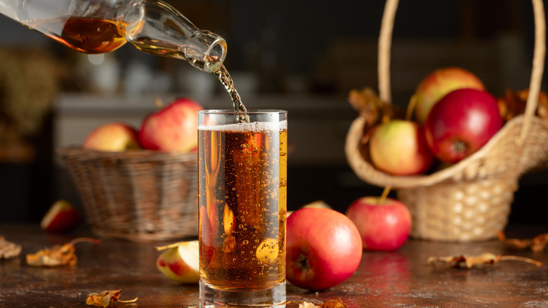 Apple cider being poured into a glass with a basket of apples in the background