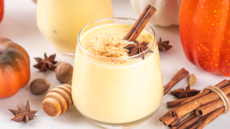 A glass of eggnog surrounded by spices