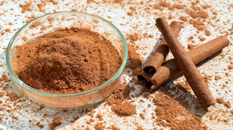 A small glass dish with cinnamon powder surrounded by sticks of cinnamon