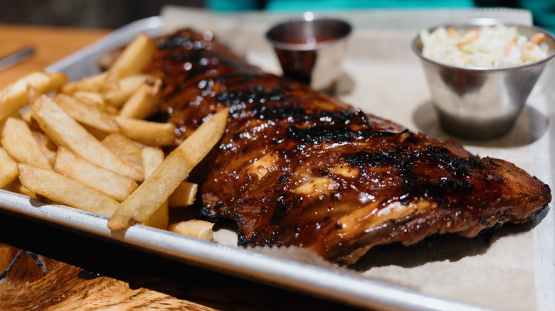 BBQ ribs on a metal plate with french fries, coleslaw and ketchup on it