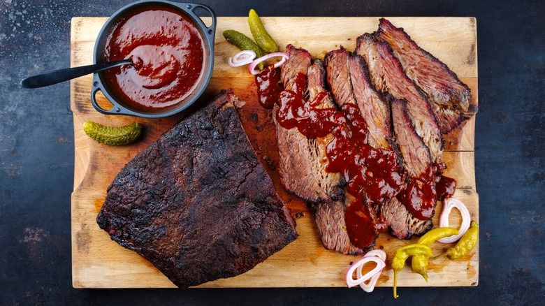 a top-down view of a Wagyu brisket on a wooden cutting board with a cup of sauce on it