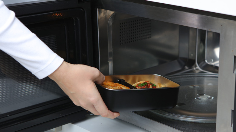 Hand putting metal tray in microwave