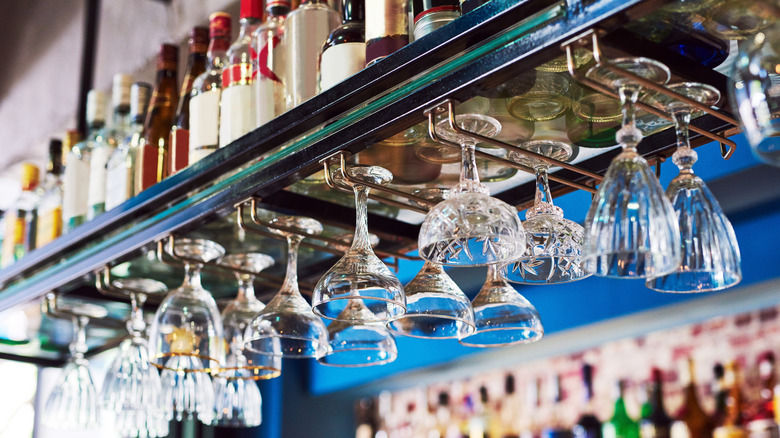 An array of bar glasses hang from a shelf filled with liquor bottles