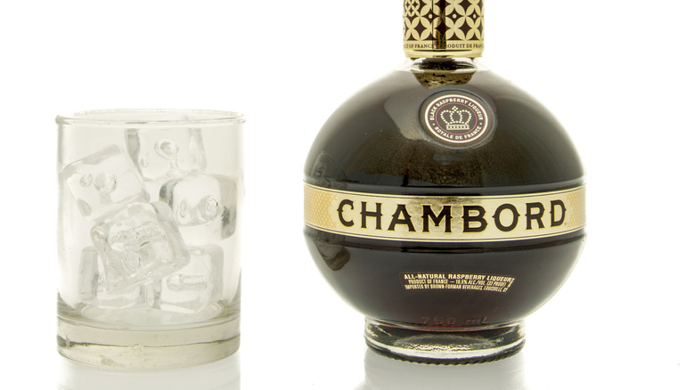 Purple bottle of Chambord next to a rocks glass filled with ice.