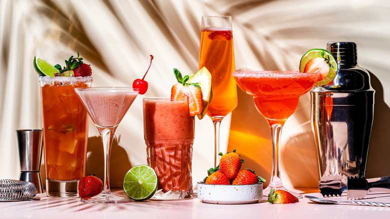 A line of five uniquely shaped glasses filled with colorful drinks and garnished with berries.