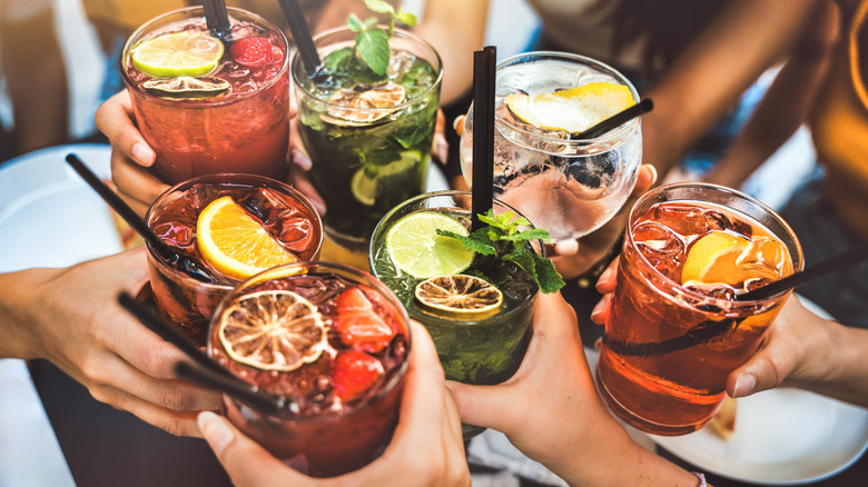 Close up of seven different cocktails clinking together.