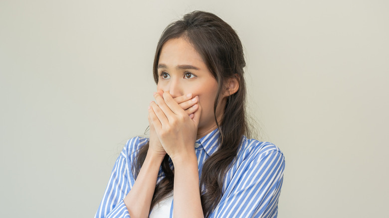 A brunette woman looks concerned and covers her mouth with both hands.