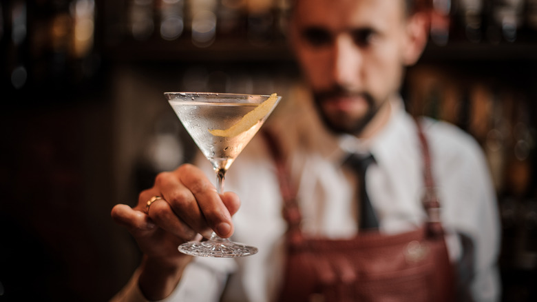 Bartender extending a martini glass filled with clear liquid.