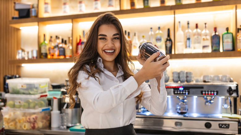 A female bartender in a white button up with a shaker.