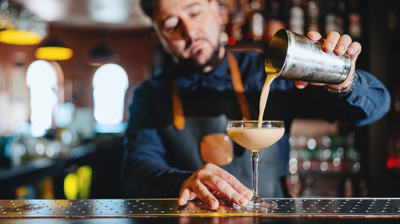 Bartender pouring a cocktail into a coupe glass.