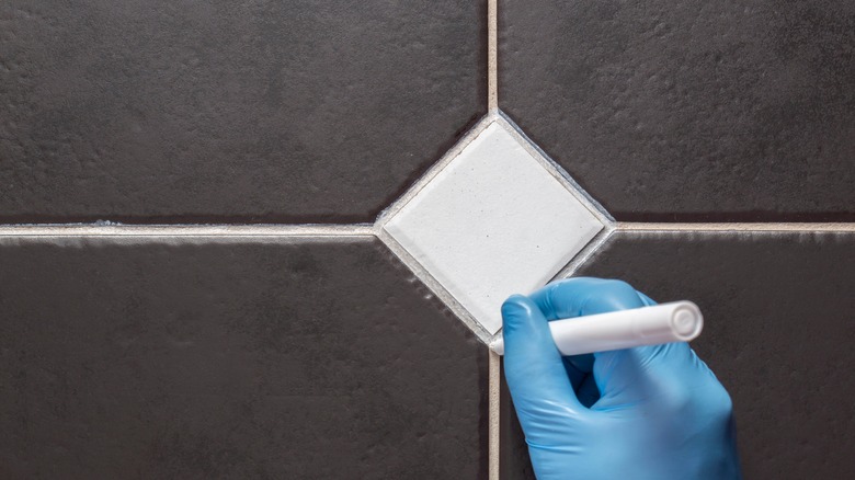 Gloved hand using grout pen on white grout between black rectangular tiles with a white diamond tile between them